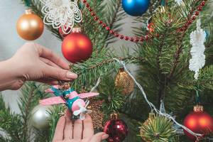 Ornamente für den Adventsbaum: Mädchen hängt einen Hirsch im Flugzeug an den geschmückten Weihnachtsbaum
