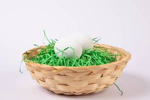 Osterkörbchen gefüllt mit zwei unbemalten Eiern auf Ostergras vor weißem Hintergrund