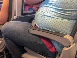 Overweight Passenger on the airplane, sitting constricted on the seat with no space