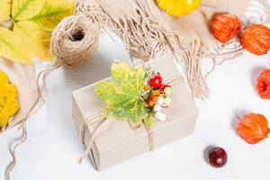 Packaged gift with yellow leaves, berries, scarf and thread on white wooden table. Family holiday concept, Thanksgiving Day