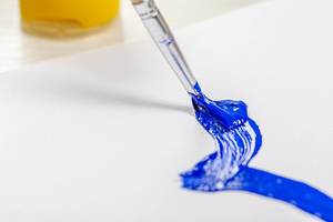 Paint brush with blue paint draws on white paper
