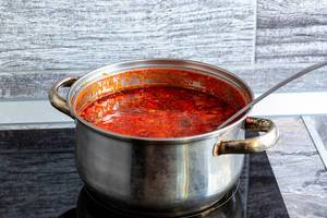 Pan on the stove with red tomato soup and ladle