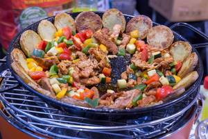 Pan with crispy potato slices, pieces of meat and colorful vegetables on low-smoke Lotusgrill