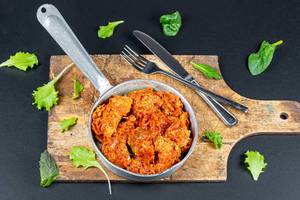 Pan with stewed fish in tomato sauce on a dark background with lettuce leaves
