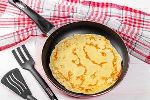 Pancake on a frying pan with a kitchen towel