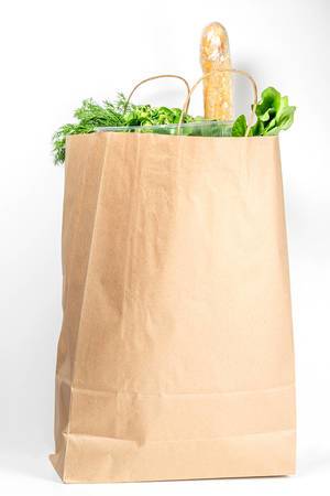 Paper bag with fresh herbs and baguette on a white background. Food purchasing concept
