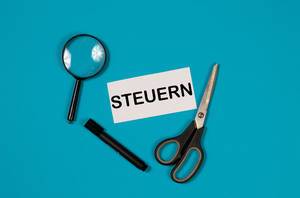 Paper with word Steuern and scissors on blue background