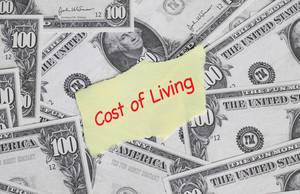 Papier mit Text COST OF LIVING (Lebenshaltungskosten) auf Hintergrund aus Banknoten