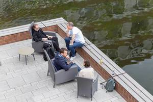 Participants of the Barcamp OMWest relaxing on rattan chairs on a veranda by the lake of the AXA building in Cologne, Germany