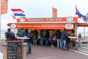 Passanten mit Winterkleidung essen an Imbissbude Boudewijns Visservice am Strand von Zandvoort, Niederlande