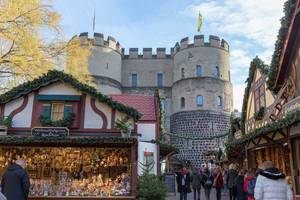 Passanten schlendern durch Weihnachtsmarkt vor alter Kölner Stadtmauer am Kölner Rudolfplatz