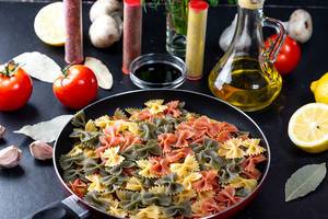 Pasta-bows with spices and fresh herbs on a black table. The concept of cooking