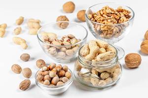 Peanuts, walnuts, pistachios and hazelnuts in glass bowls and in a jar on a white background (Flip 2020)