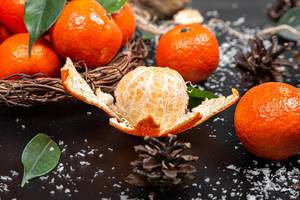 Peeled and whole tangerines on black background with leaves and snow (Flip 2019)