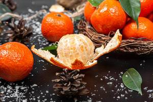 Peeled and whole tangerines on black background with leaves and snow