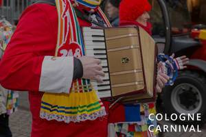 People in carnival costumes play the accordion during the carnival procession, next to the picture title "Cologne Carnival"