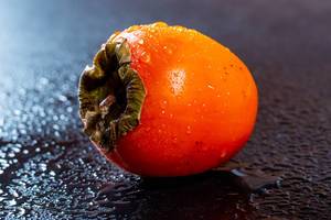 Persimmon fruit on dark background with water drops .