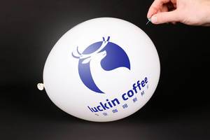 Person bringt einen Luftballoon mit Luckin Coffee Logo mit einer Stecknadel zum platzen mit schwarzem Hintergrund