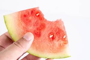 Person holding a Slice of Watermelon with a Bite on White Background