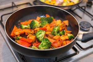 Pfanne mit gedünstetem Gemüse wie Brokkoli, Paprika und Kartoffeln auf Gasherd