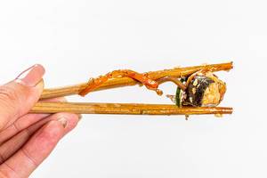 Piece tuna in sauce close up in chopsticks holding a woman on white background