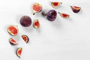 Pieces of fresh figs and whole fruit on a white wooden background with water drops
