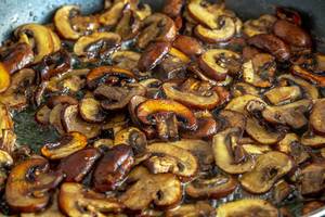 Pieces of mushrooms are fried in oil in a frying pan