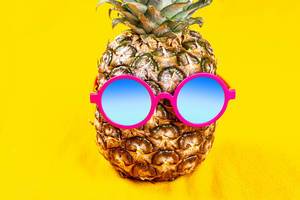 Pineapple in round sunglasses on a yellow background