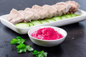 Pinke Meerrettich-Soße und in Scheiben geschnittene gekochte Zunge vom Schwein neben Gemüse, vor schwarzem Hintergrund angerichtet
