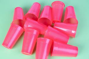Pinke Plastikbecher für Einmalgebrauch vor kontrastreichem grünem Hintergrund