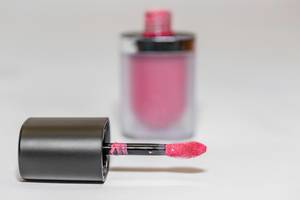 Pinker Lipgloss mit Applikationspinsel vor weißem Hintergrund