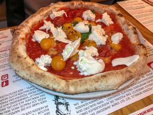 Pizza in Restaurant mit dickem knusprigem Rand, Tomaten und nicht geschmolzenem Mozzarella Käse