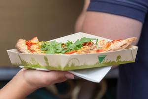 Pizzastück mit Rucola auf kompostierbarem Pappteller von Essensstand am Tomorrowland 2019