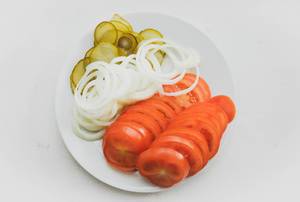 Plate with sliced tomato, onion, and pickles