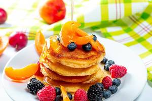 Plate with tasty pancakes and berries, honey pours from the top