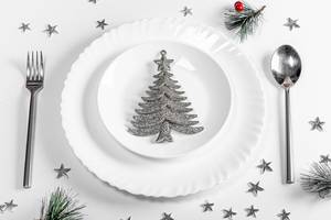 Plates with spoon and fork on a white table with Christmas silvery decor