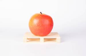 Praller roter Apfel auf kleiner Holzpalette als Symbol für Transport von Früchten und Gemüse