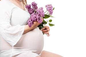 Pregnant girl sitting in a white dress with a bouquet of lilacs
