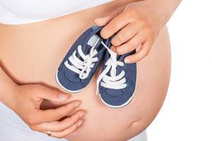 Pregnant woman holds small blue shoes on the her abdomen. Concept of happy pregnancy and expectation