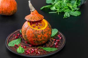 Pumpkin puree and pomegranate in fresh pumpkin with spinach leaves on black background (Flip 2019)