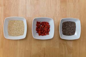 Quiona, Goji Berries and Chia Seeds Superfoods in White Bowls on Wooden Table