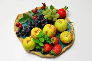 Quitten mit Weintrauben, Erdbeeren und Hagebutten auf Obstschale aus Ton