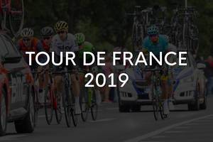 Radrennfahrer beim Radsportevent zwischen Teamautos und der Aufschrift "Tour de France 2019"