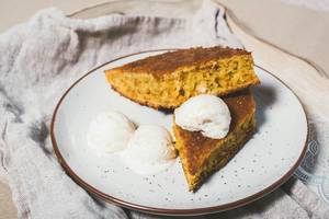 Rautenförmige Stücke vom Möhrenkuchen mit Vanilleeis auf einem Teller und Leinentuch