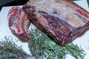Raw, deep-frozen meat with green herbs on a kitchen board
