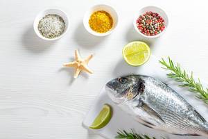 Raw fresh Dorada on a white wooden table with spices, rosemary, lime slices and starfish (Flip 2019)