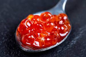 Red caviar in the silver spoon on a black background