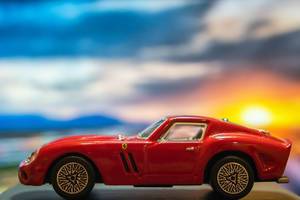 Red Ferrari toy car on platform with sunset background