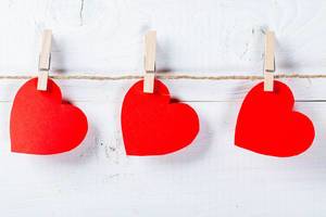 Red hearts hanging on clothespins on white wooden background