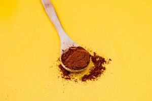 Red pepper spice on wooden spoon. Yellow background